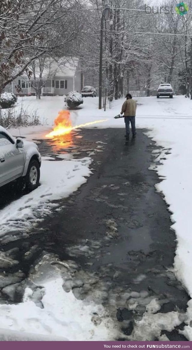 A guy is using a flame thrower to clear snow off his street