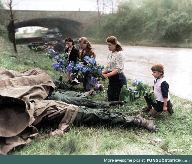 Russian women liberated from a slave labor camp lay flowers at the feet of three soldiers