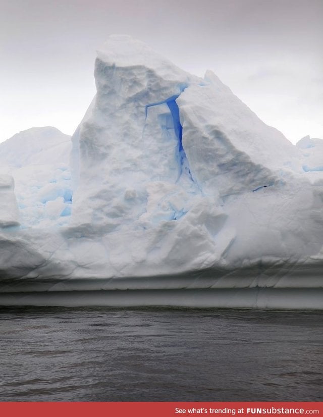 A bright, brilliant blue glows from within an Antarctic iceberg