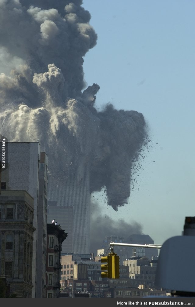 Two men upon a rooftop are dwarfed by the collapsing World Trade Center on September 11