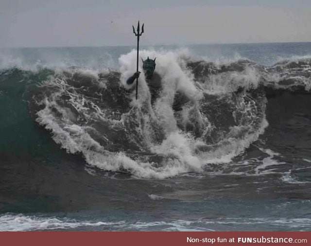 A wave engulfs the statue of Neptune on Melenara Beach, Gran Canaria