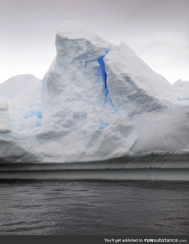 A bright brilliant blue glows from within an Antarctic iceberg
