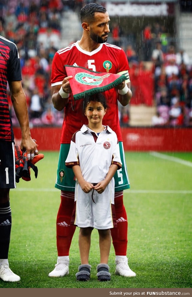 Moroccan soccer team captain Benatia covering a little girl's head from the rain