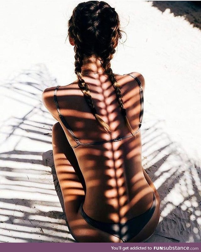 Sunlight reflects from a coconut branch on to a girls back, looking like a spine