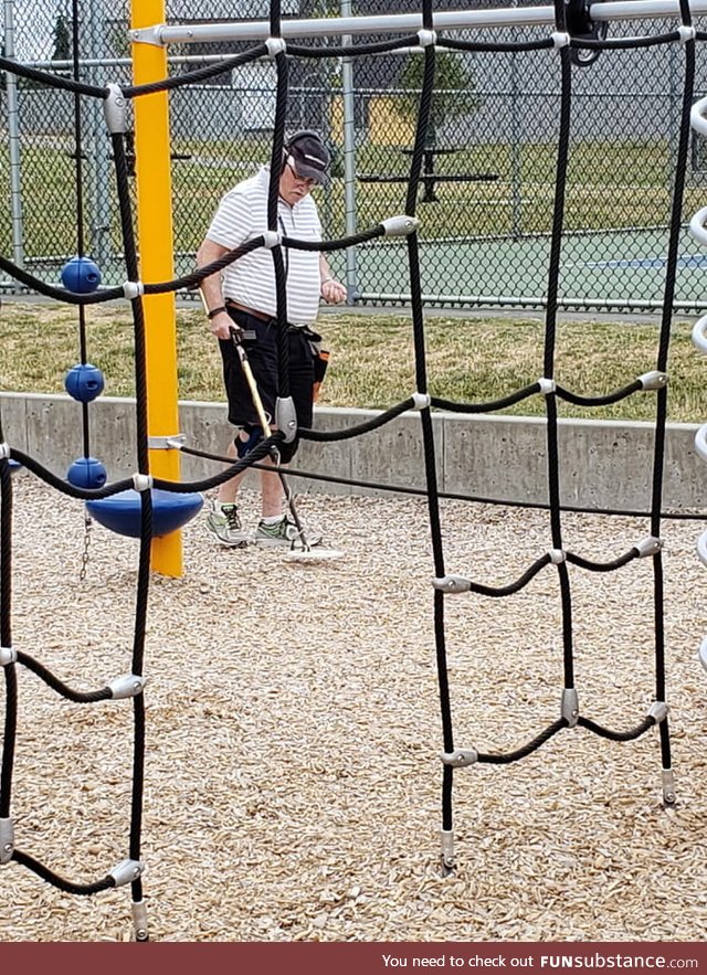 Guy using his metal detector at a playground to collect small pieces of metal that could