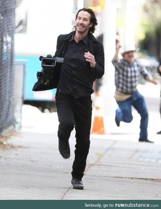 A photo of Keanu Reeves running away with a camera he took from a Paparazzi guy is