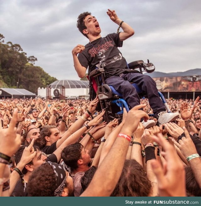 A guy in a wheel chair enjoys crowd surfing at a heavy metal festival in spain