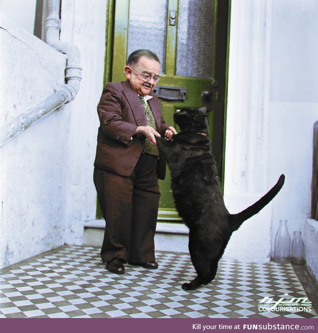 Henry Behrens, the smallest man in the world dances with his pet cat in the doorway of