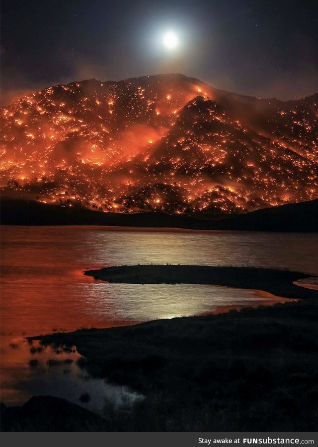 The moon rises above a mountain in California completely covered in wildfires