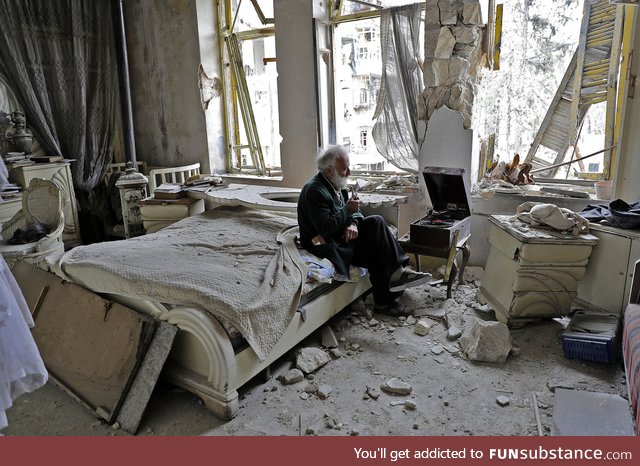Syrian man listens to music on his hand-cranked gramophone in his destroyed bedroom,