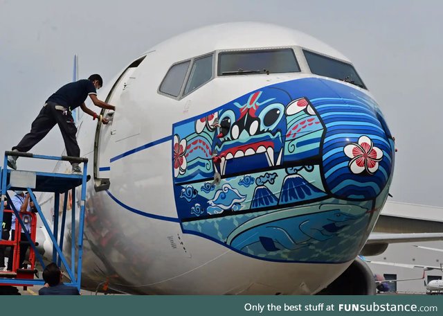 A worker outside a Garuda Indonesia Boeing with a new face mask design to promote COVID