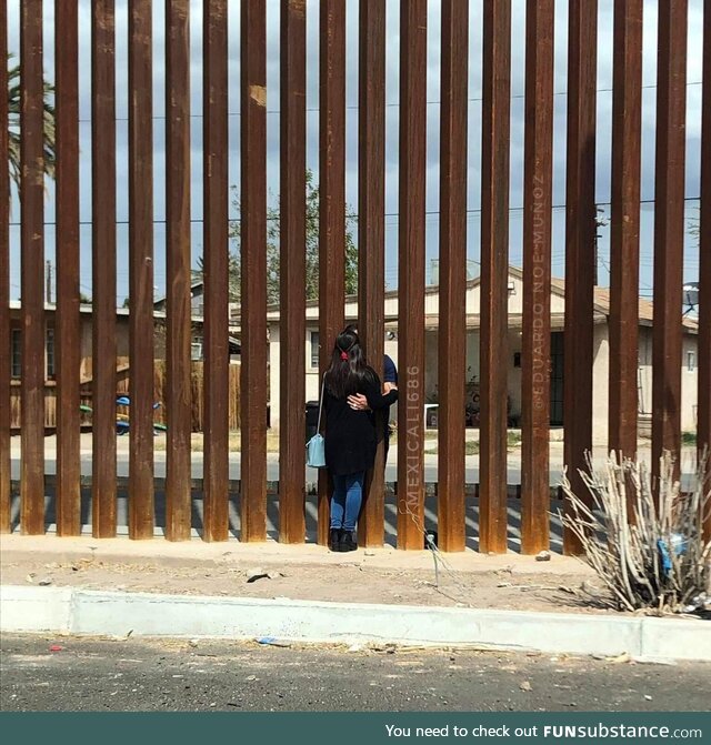 A couple hugging through the border wall