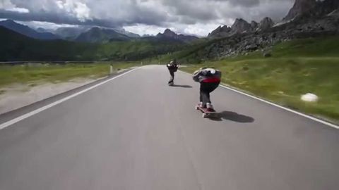 Three Skateboarders Passing Cyclists as They Descend the Alps