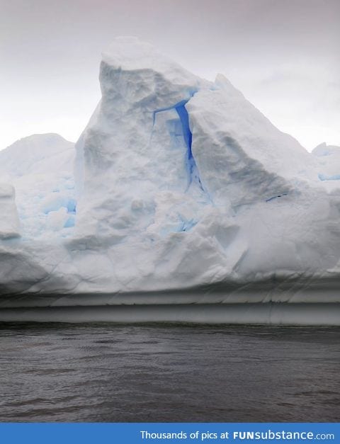 A bright, brilliant blue glows from within an Antarctic iceberg