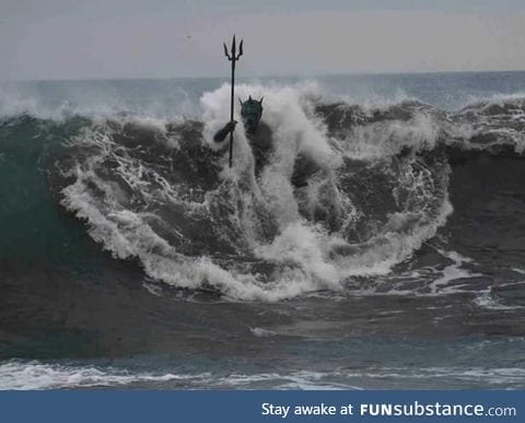A wave engulfs the statue of Neptune on Melenara Beach, Gran Canaria