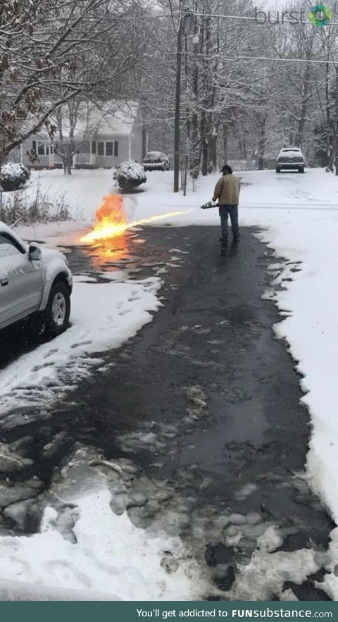 A guy is using a flame thrower to clear snow off his street