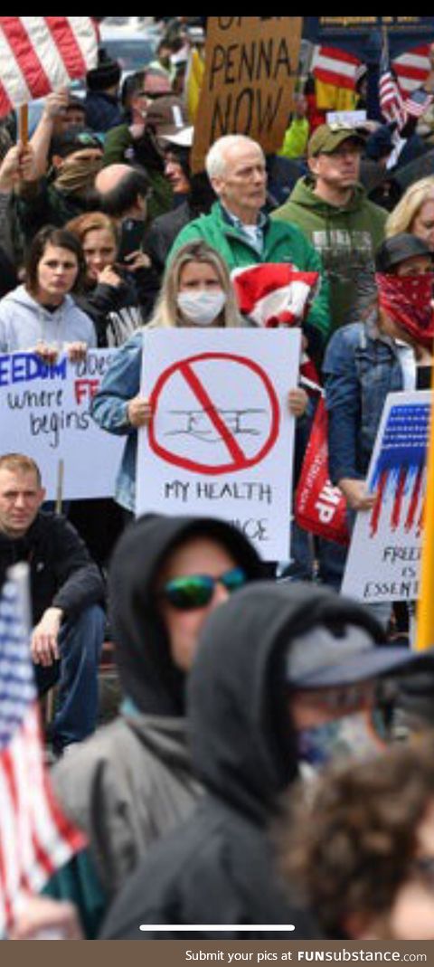 Anti stay at home protester holding an anti mask sign while wearing mask in crowd