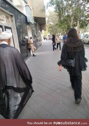 In an act of defiance, an Iranian women walk without the mandatory hijab next to mullahs