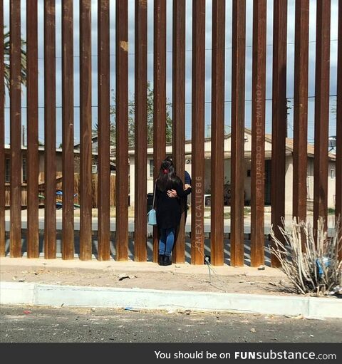 A couple hugging through the border wall