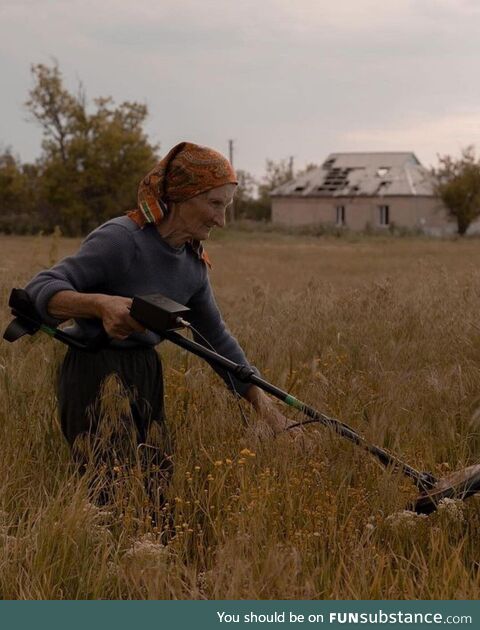 A Ukrainian woman, using a metal detector, is searching for mines on her farm