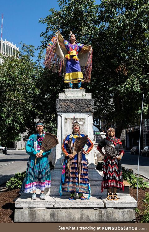 Indigenous women in traditional regalia stand over a former monument to Columbus in