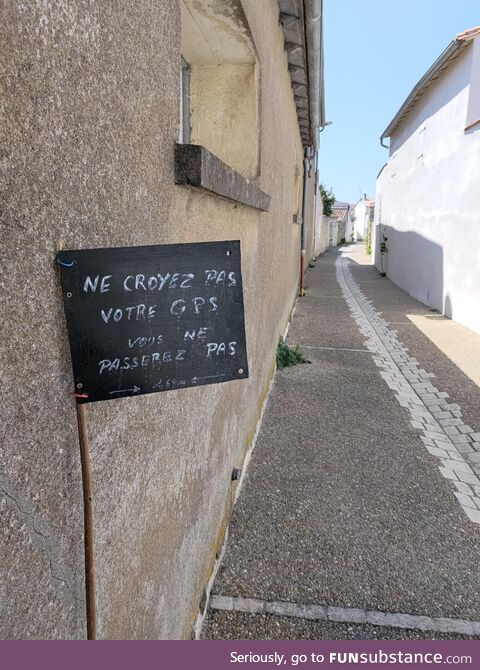 This sign reading "Don't believe your GPS, you can't fit through here" on a tiny street