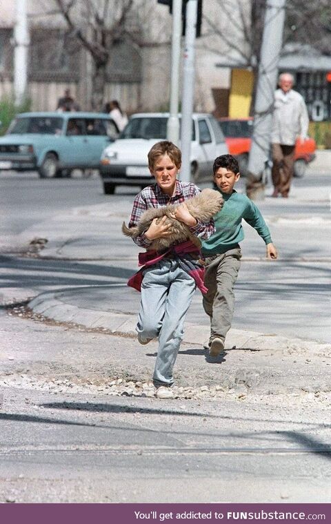A boy carrying his dog while crossing the infamous “Sniper Alley” - April 1995